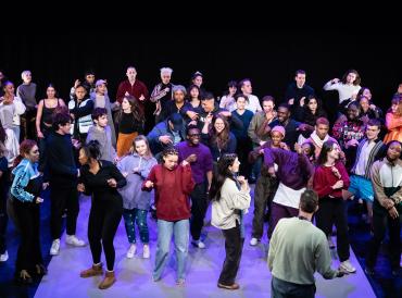 A large group of LAMDA professional acting students on stage in the Sainsbury Theatre during the 2023 Graduating Actors showcase