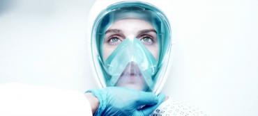 A futuristic mask is placed on a woman by a medic in a white environment 