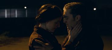 A woman and a man embrace in a car park at night