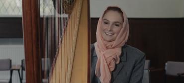 A women in a head scarf sits next to a harp
