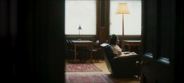 A figure seated in a chair is seen through a doorframe