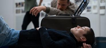 A woman lies on the floor resting next to a suitcase, while a man lounges next to her