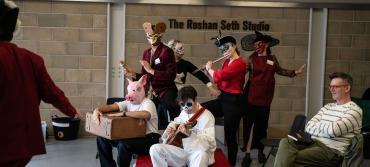 A group of MFA Professional Acting students rehearsing a scene in the Roshan Seth Studio for Romeo & Juliet as part of the the Shakespeare In Schools tour. Some students are playing instruments and are in masks.