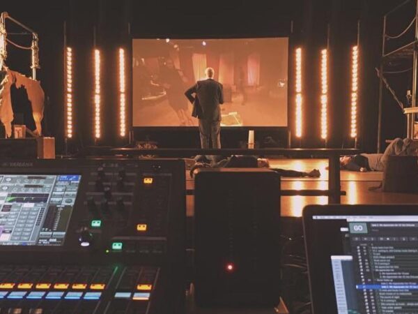 Sound and lighting control desk facing a stage with performers and a large screen backdrop