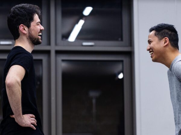 Two men laughing together while chatting outside a building with large windows