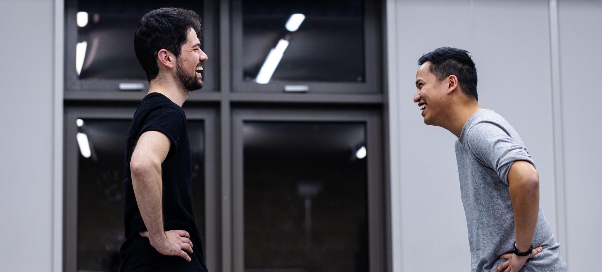 Two men laughing together while chatting outside a building with large windows