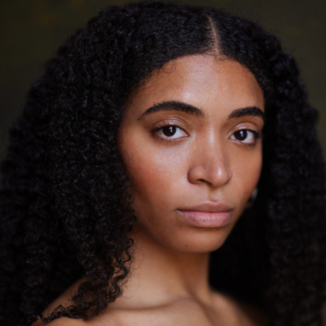Close-up portrait of a woman with long curly dark hair, looking directly at the camera