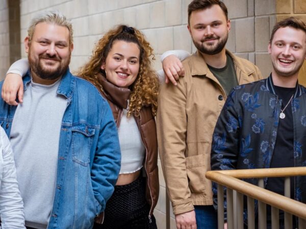 Group of six colleagues standing together on a staircase, smiling for the camera