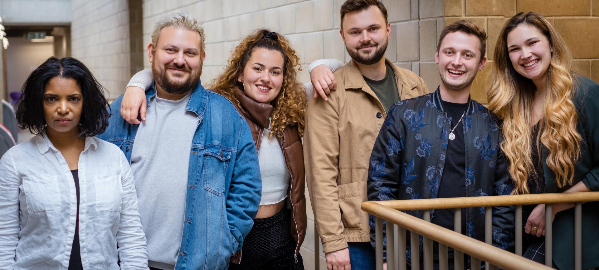 Group of six colleagues standing together on a staircase, smiling for the camera