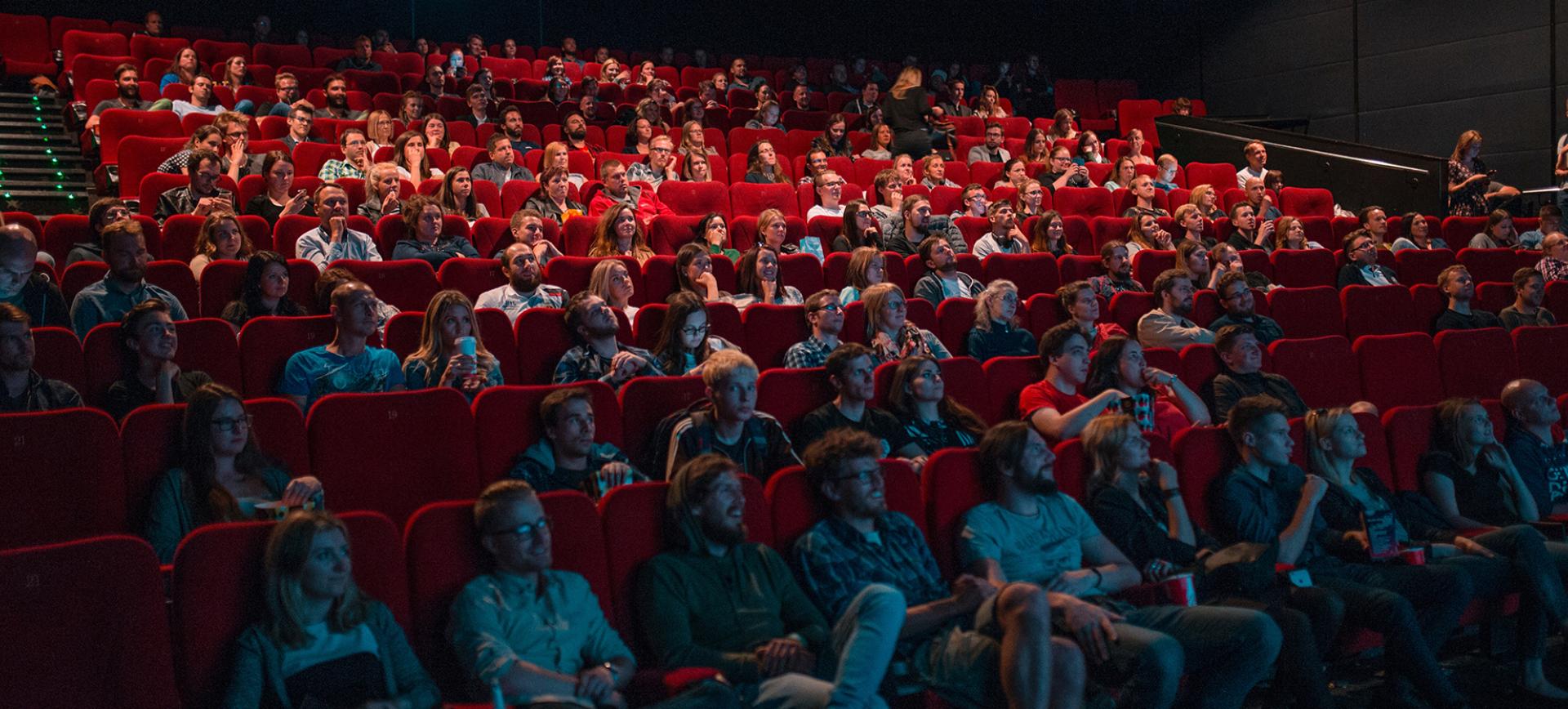 A packed cinema audience seated in red seats, watching a film attentively