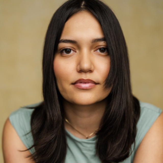Portrait of a woman with long dark hair, wearing a sage green top, looking directly at the camera