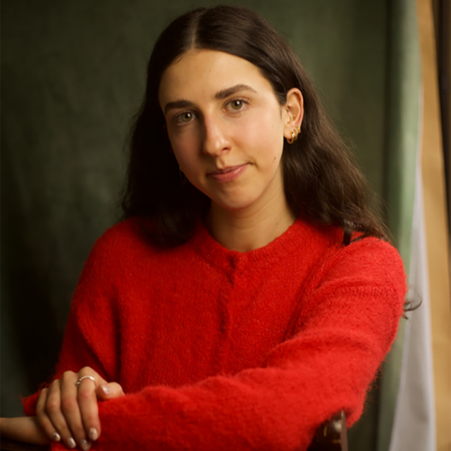 Woman with long dark hair wearing a red knitted jumper, sitting with arms crossed