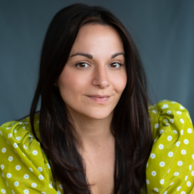 Portrait of a woman with long dark hair, wearing a green floral-print top, smiling gently