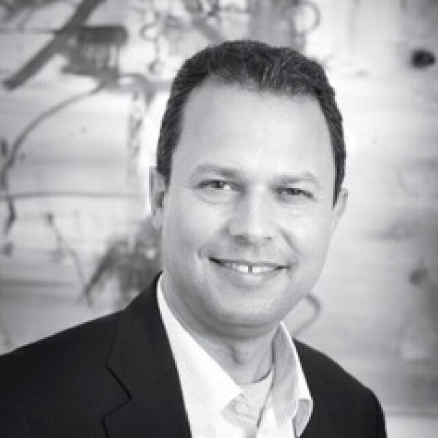 Black and white portrait of a smiling man with short dark hair, wearing a dark jacket over a light shirt
