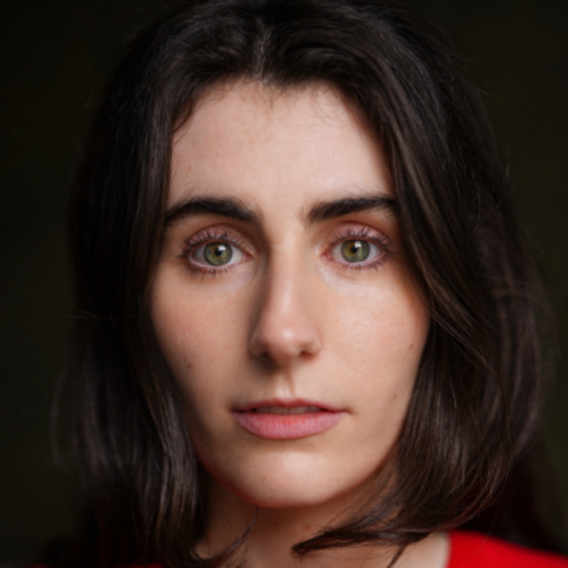 Close-up portrait of a woman with dark hair and green eyes, looking directly at the camera with a neutral expression