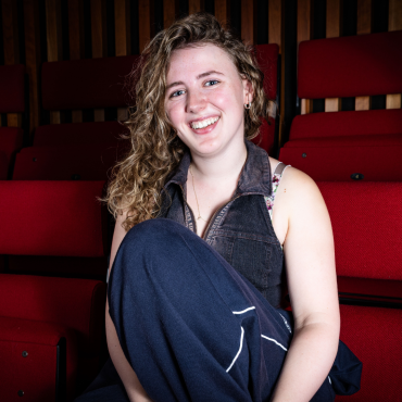 Young woman with curly hair smiling, seated among red theatre seats