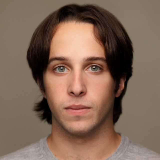 Headshot of a young man with shoulder-length brown hair and green eyes, wearing a grey top, against a neutral grey background
