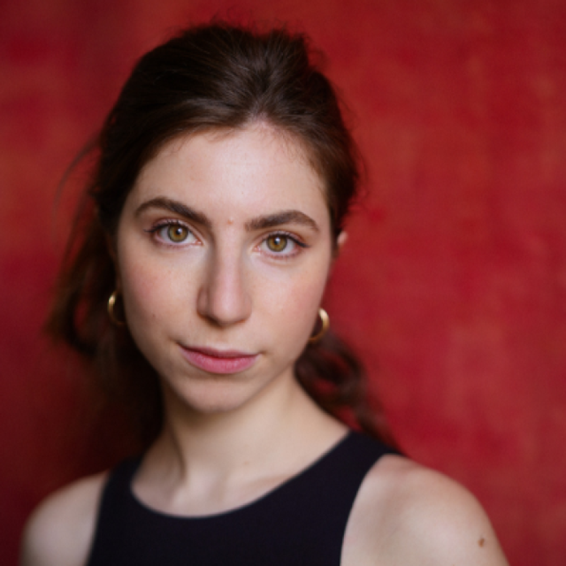Portrait of a young woman with dark hair and gold hoop earrings against a red background