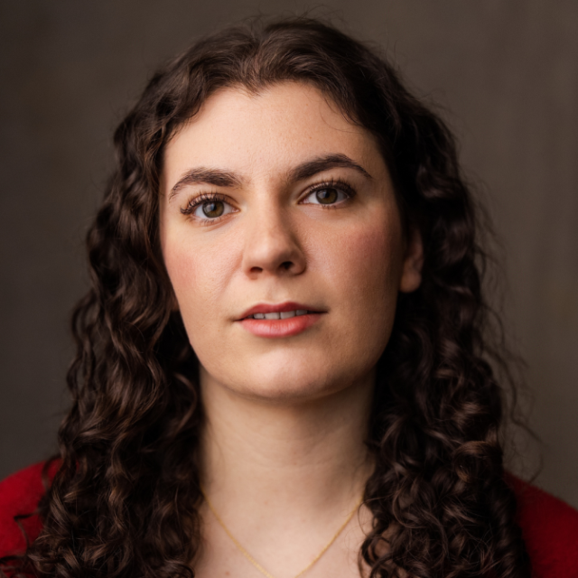 Close-up portrait of a woman with long curly brown hair, wearing a red top and a thin necklace