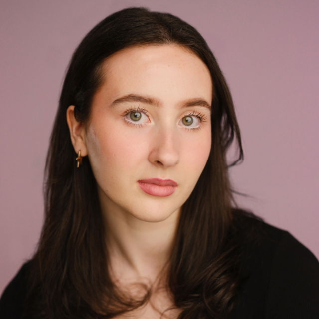 Portrait of a young woman with long dark hair, looking directly at the camera against a lilac background