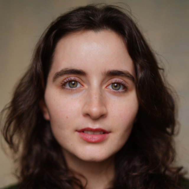 Close-up portrait of a young woman with wavy dark brown hair and green eyes, looking directly at the camera