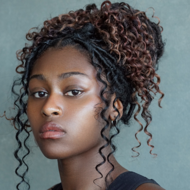 Woman with curly hair styled in a high updo with braided sections, looking directly at the camera
