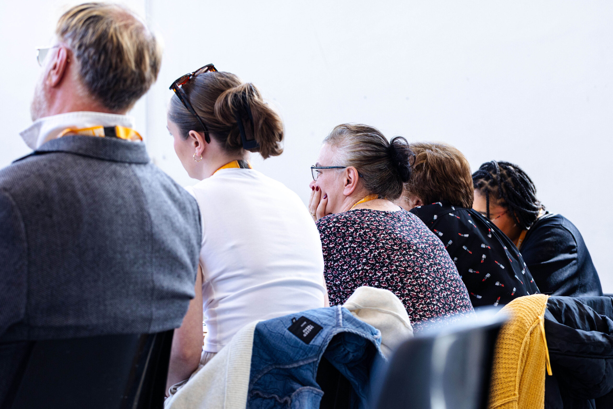 Seated audience members wearing event lanyards, seen from behind, watching attentively
