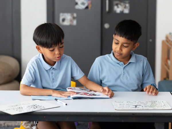 Two learners sit at a desk reading a book together