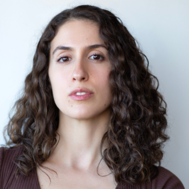 Woman with long curly dark hair looking directly at the camera against a plain light background