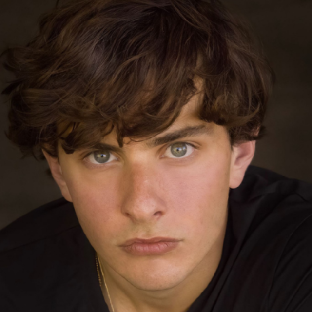 Close-up portrait of a young man with curly brown hair and green eyes, wearing a black top