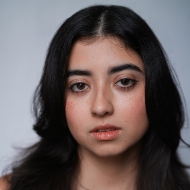 Close-up portrait of a young woman with long dark hair, looking directly at the camera with a neutral expression