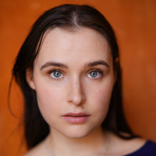 Close-up portrait of a young woman with dark hair and blue eyes against an orange background