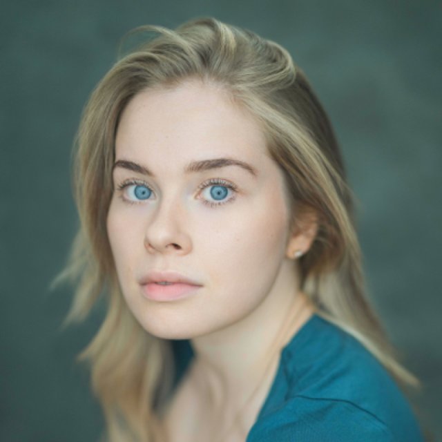 Close-up portrait of a young woman with blonde hair and blue eyes, wearing a teal top against a dark green background