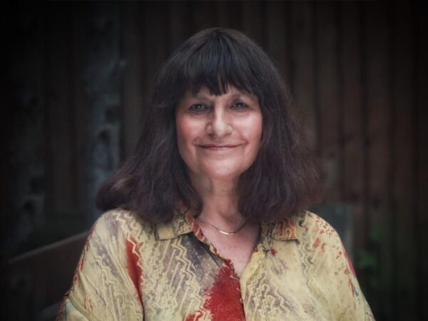 Woman with dark shoulder-length hair and a fringe, smiling, wearing a patterned red and gold shirt
