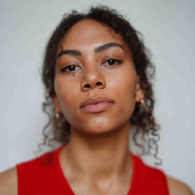 Close-up portrait of a woman with curly hair and a neutral expression, wearing a red top