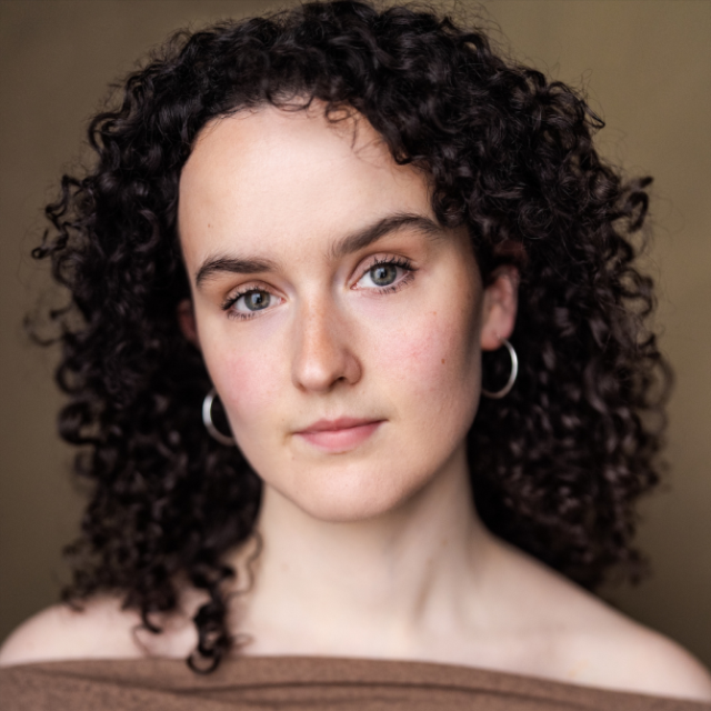 Close-up portrait of a young woman with curly dark hair and hoop earrings, looking directly at the camera