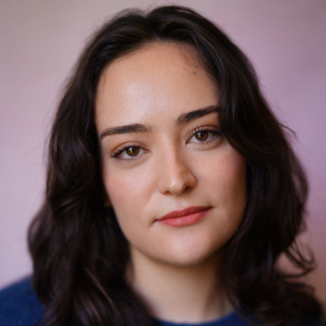 Headshot portrait of a woman with long wavy dark hair, looking directly at the camera