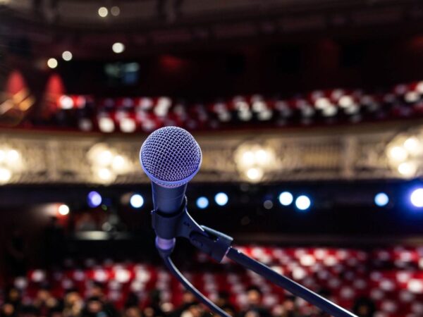 Close-up of a microphone on stage facing an empty theatre auditorium with red seating and stage lights