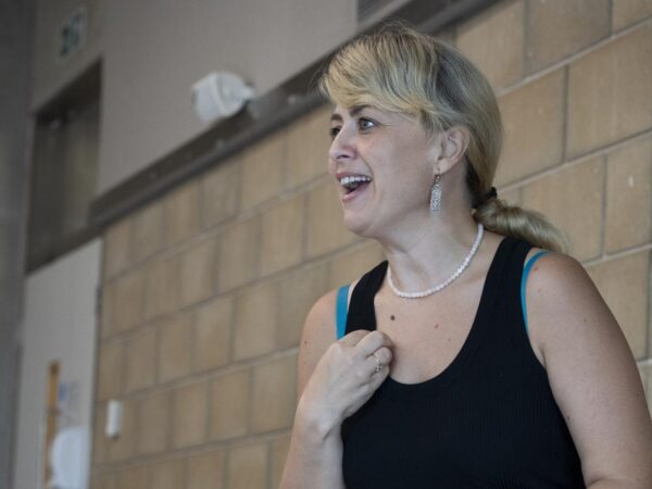 Woman with blonde hair and a pearl necklace smiling and talking, wearing a black vest top