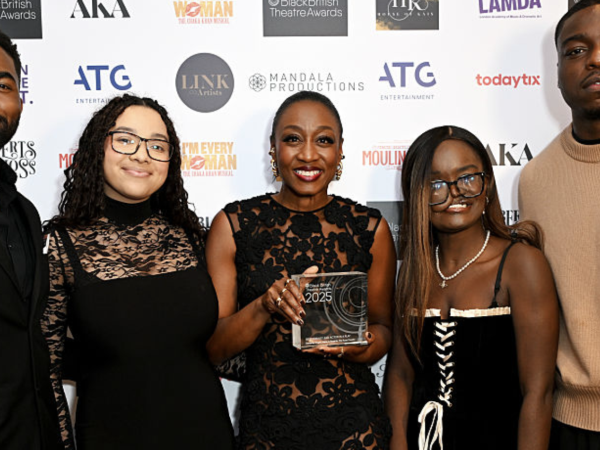 Woman holding a Black British Theatre Awards 2025 trophy, posing with four others at the event step-and-repeat