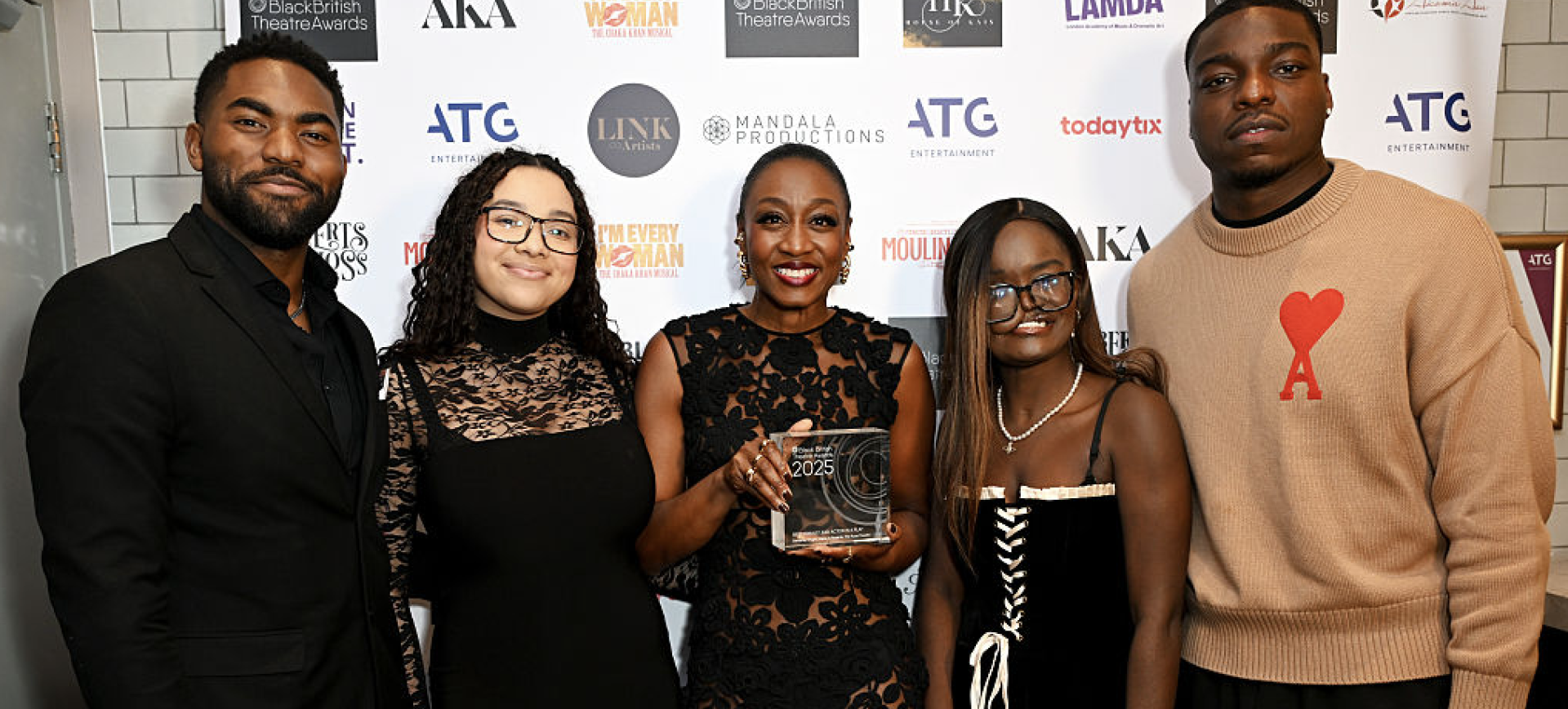 Woman holding a Black British Theatre Awards 2025 trophy, posing with four others at the event step-and-repeat