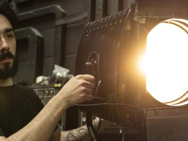 Man adjusting a large illuminated stage spotlight backstage in a theatre