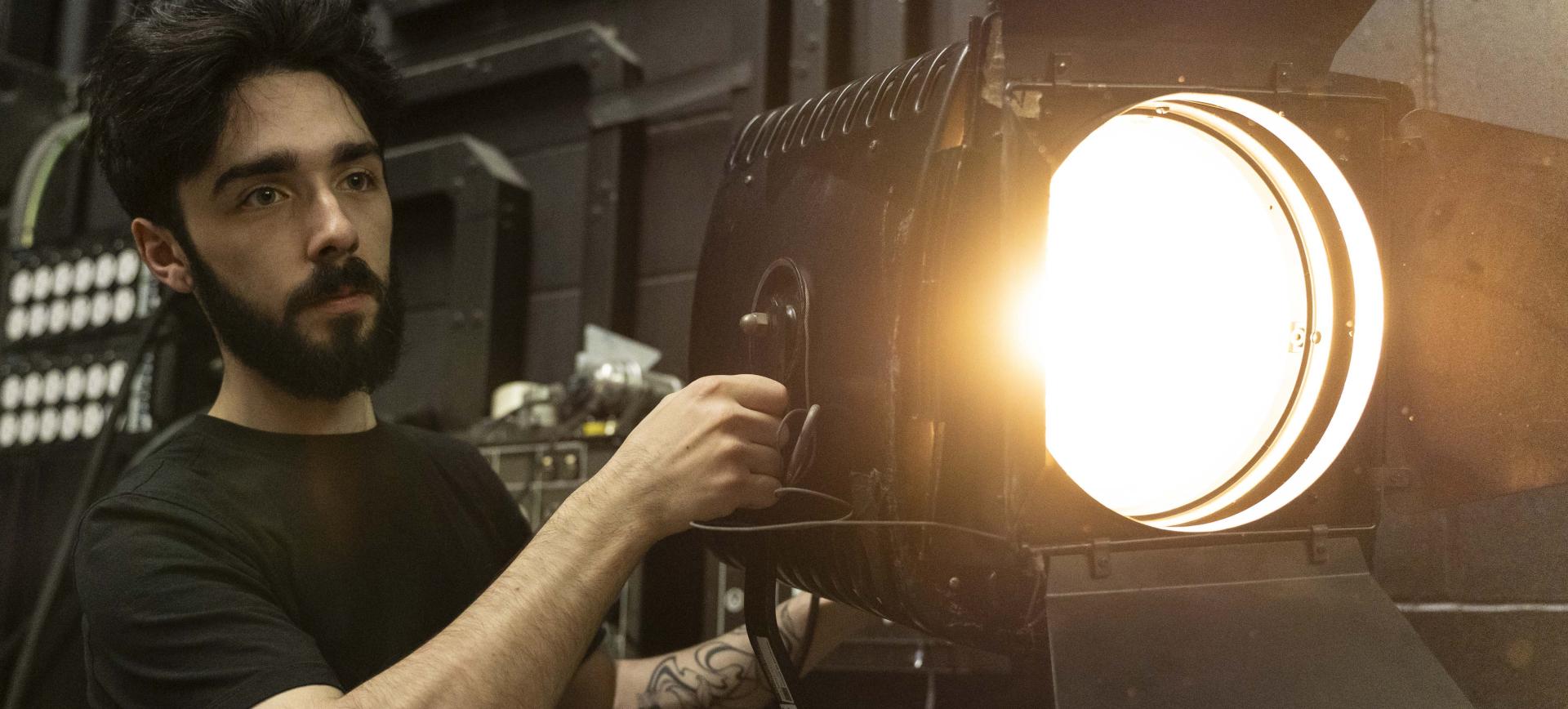 Man adjusting a large illuminated stage spotlight backstage in a theatre