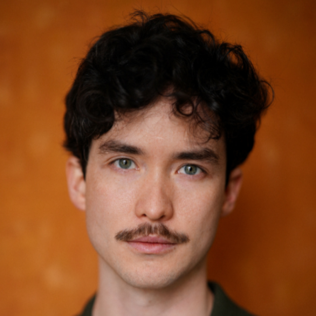 Portrait of a young man with curly dark hair, green eyes and a moustache, against an orange background