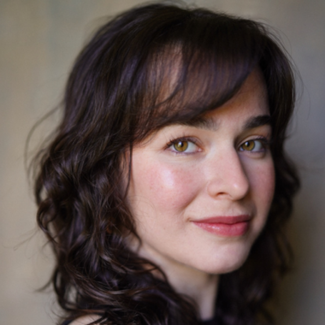 Close-up portrait of a woman with curly dark hair and hazel eyes, smiling slightly