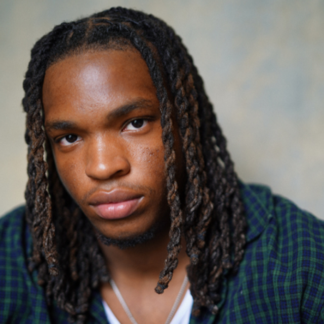 Close-up portrait of a young man with long dreadlocks wearing a green and navy plaid shirt