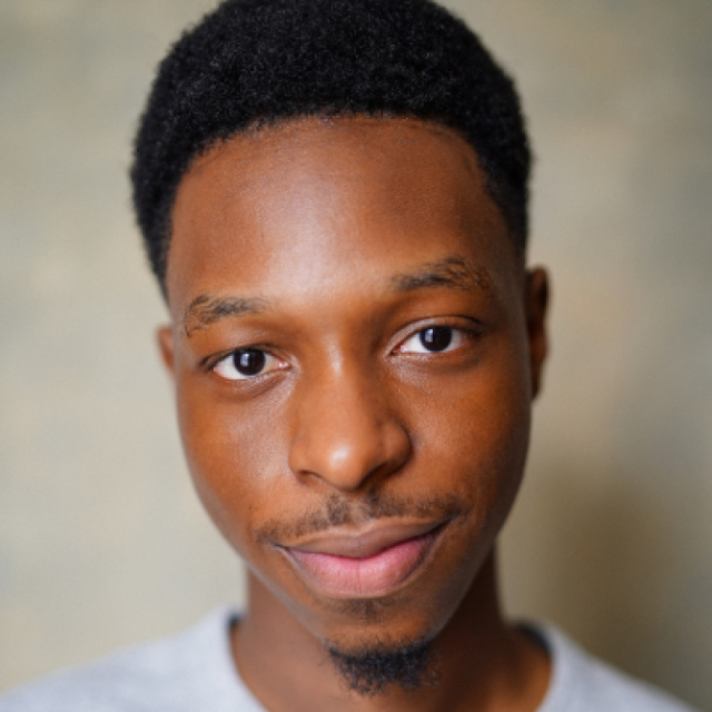 Close-up portrait of a young man with short black hair, smiling slightly at the camera