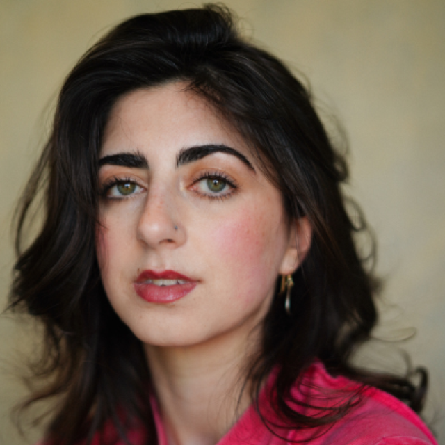 Close-up portrait of a woman with dark wavy hair, wearing a pink top and gold earrings