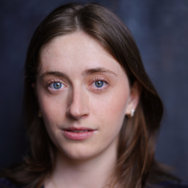 Headshot of a young woman with brown hair and blue eyes, looking directly at the camera