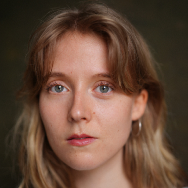 Close-up portrait of a young woman with wavy blonde hair and blue eyes, looking directly at the camera with a neutral expression